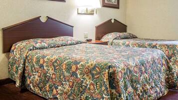 A hotel room with two beds, floral-patterned bedding, a nightstand, a lamp, and framed floral artwork on the walls.