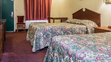 A hotel room with two beds, a chair, a desk, and a door.