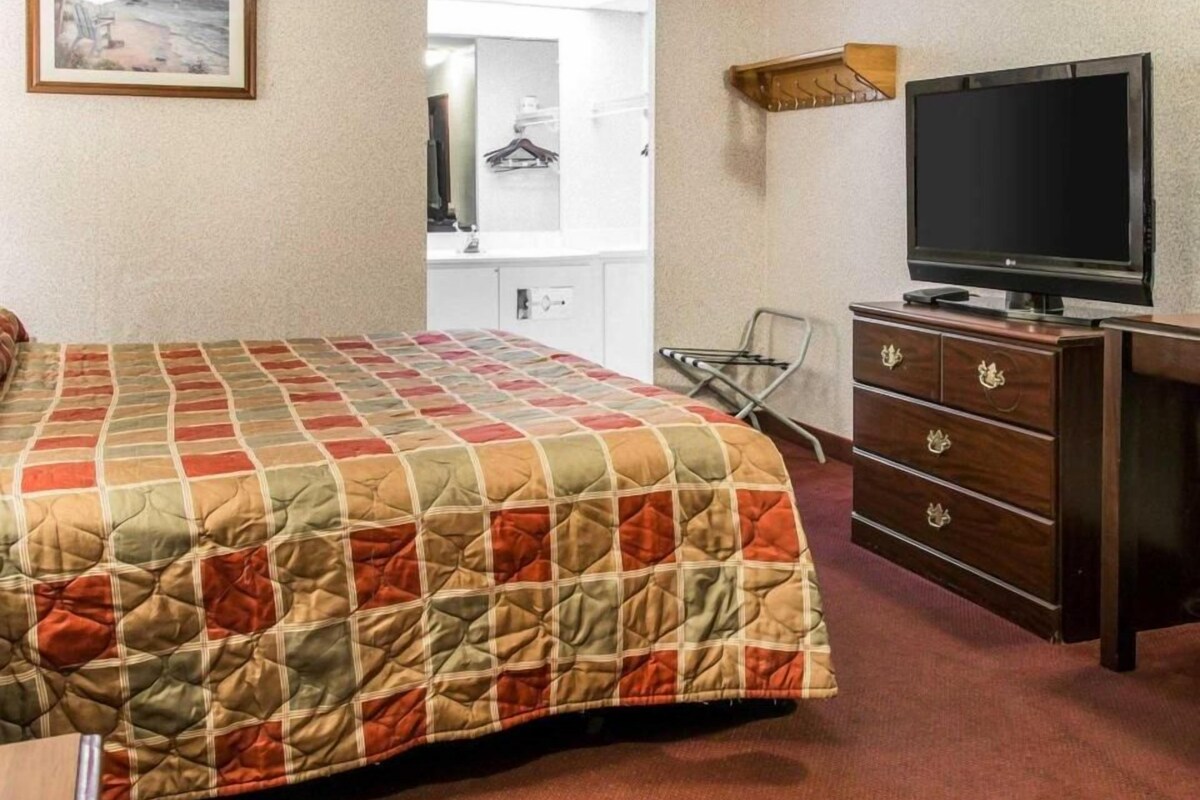 Habitación de hotel con cama, televisión, cómoda, espejo y perchero.