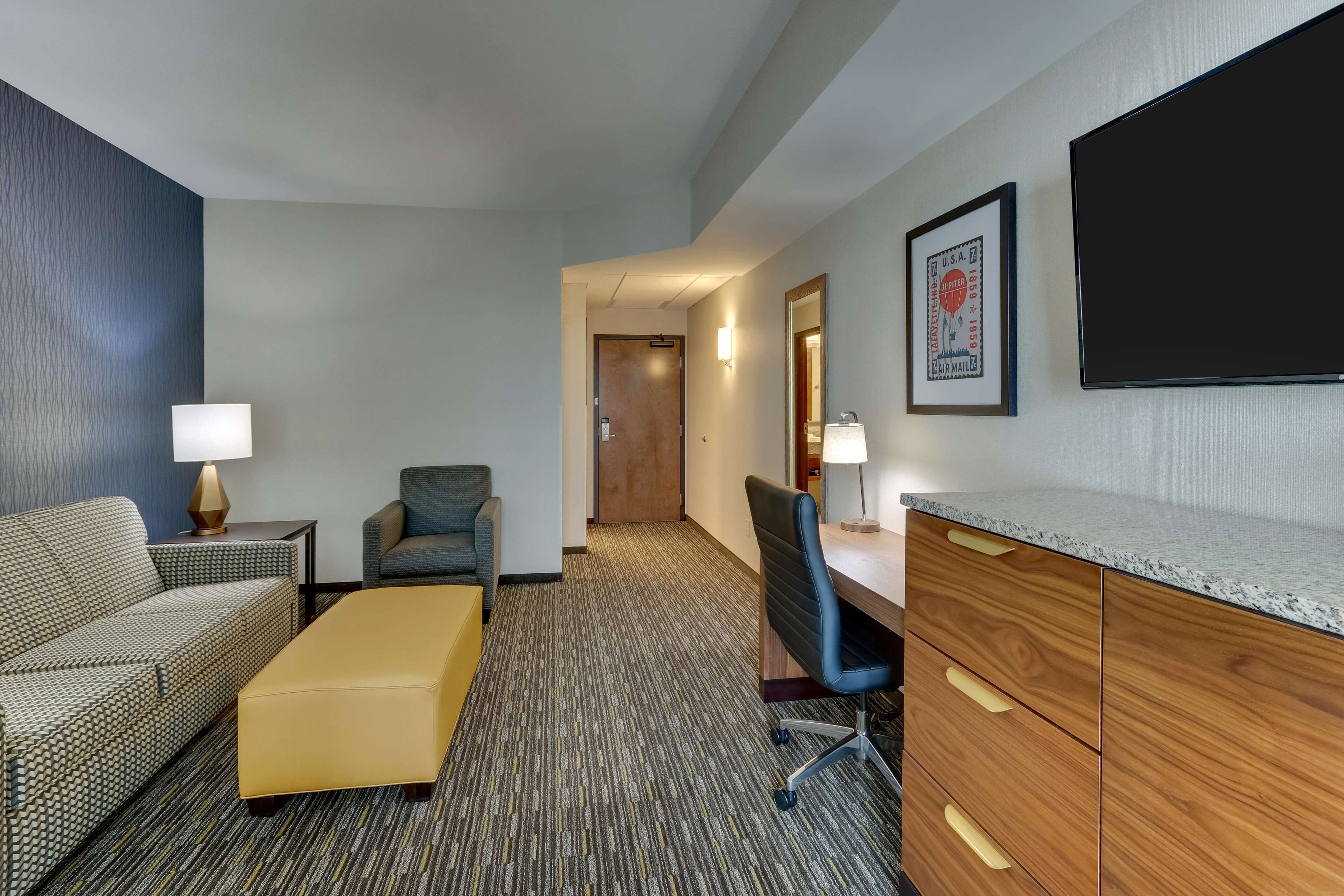 Habitación de hotel con sofá, sillón, escritorio y un espejo grande.