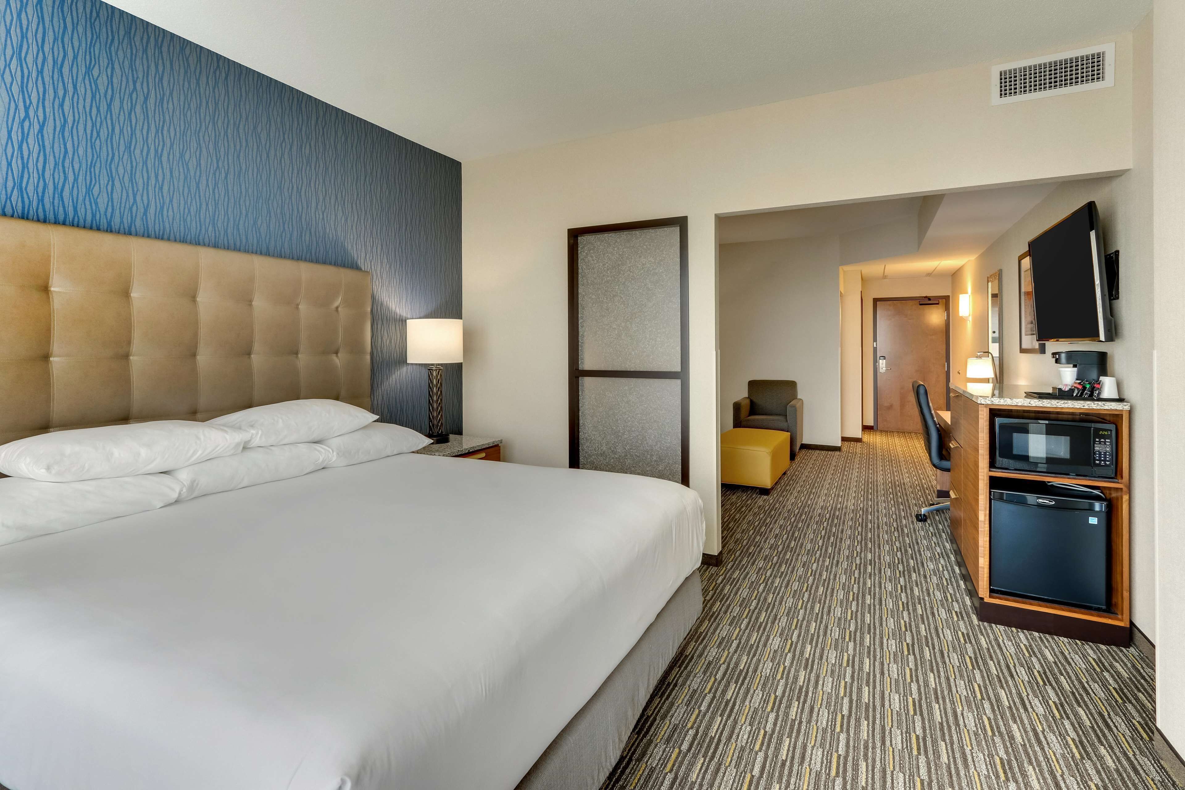 A hotel room with a large bed, a desk with a computer, a microwave, and a small seating area.