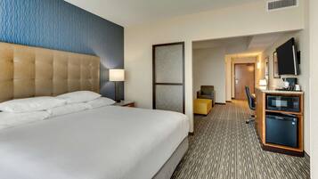 A hotel room with a large bed, a desk with a computer, a microwave, and a small seating area.