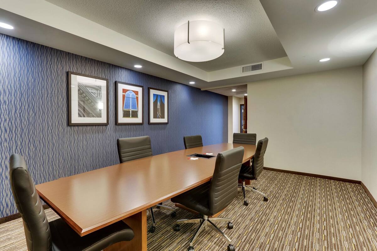 A conference room with a long table, four chairs, and framed pictures on the wall.