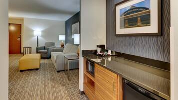 A hotel room with a kitchenette, a sofa, a small table, and a framed picture on the wall.