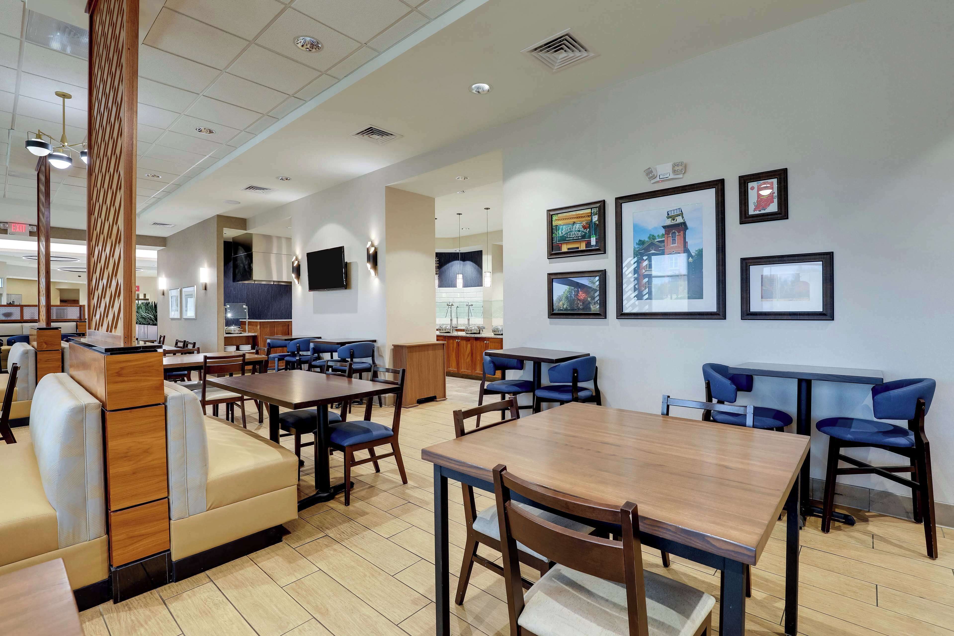 A spacious restaurant with high tables and booths, framed artwork on the walls, and a modern ceiling design.