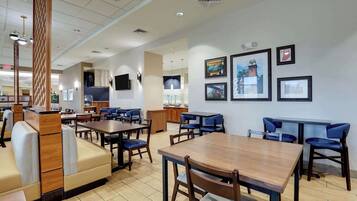 A spacious restaurant with high tables and booths, framed artwork on the walls, and a modern ceiling design.