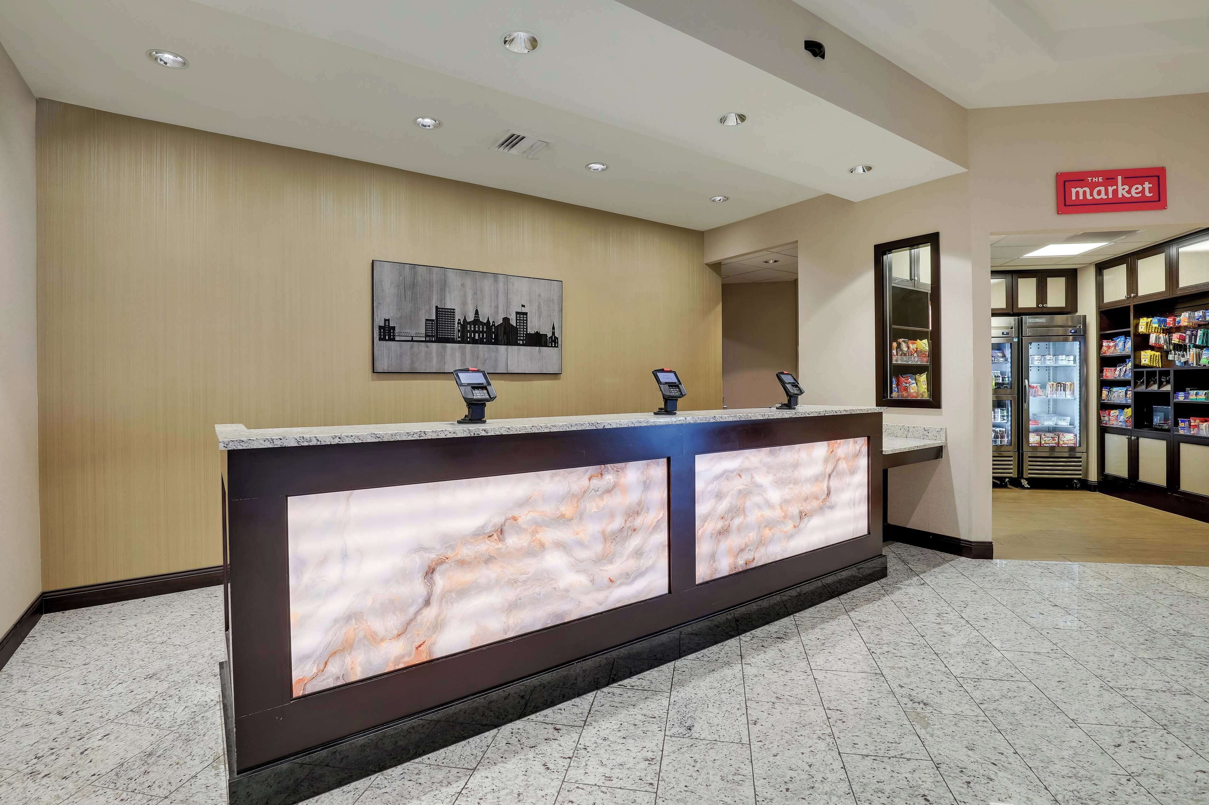 A hotel reception area with a marble counter, a cityscape painting, and a 'The Market' sign.
