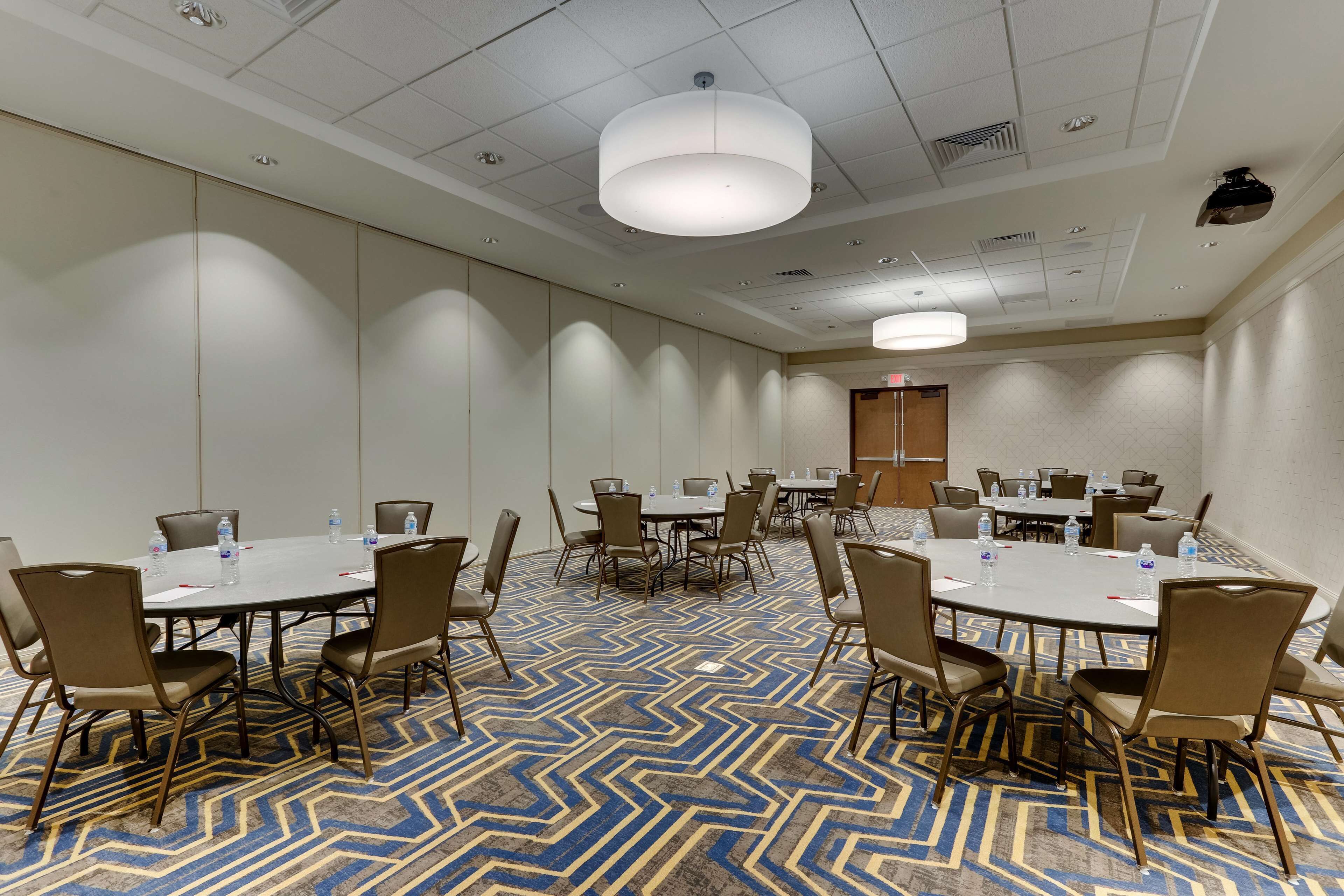 A conference room with multiple tables and chairs, equipped with water bottles, and a patterned carpet.