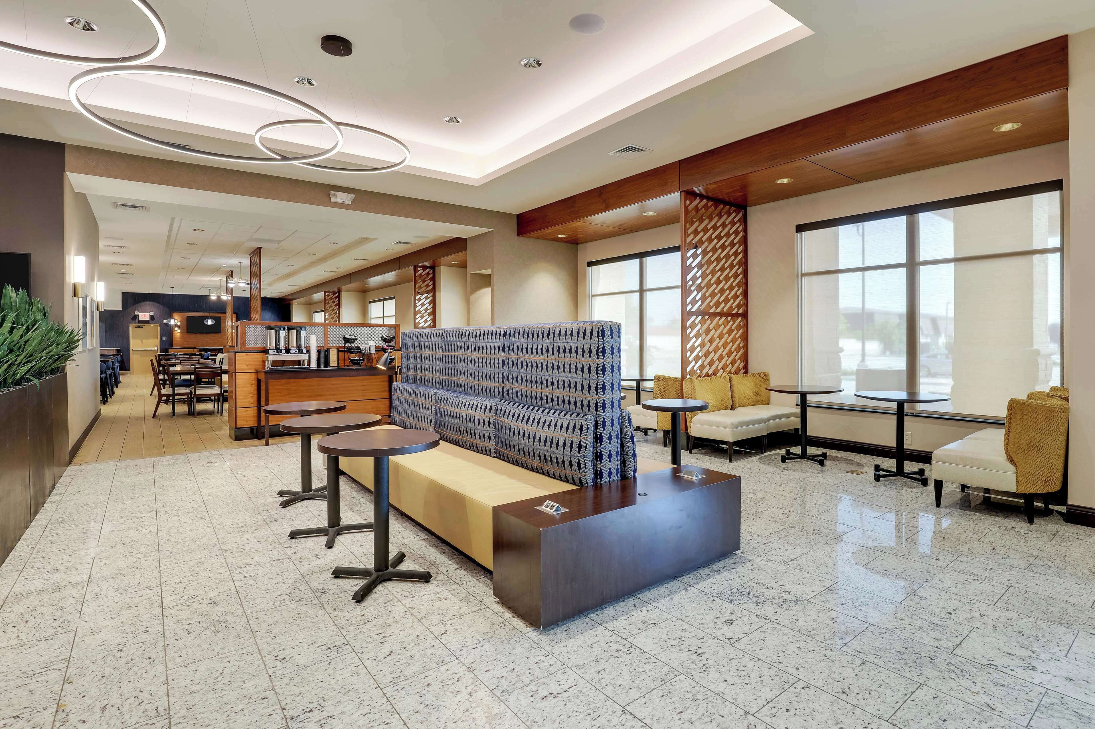 A modern hotel lobby with a reception desk, seating area, and large windows.