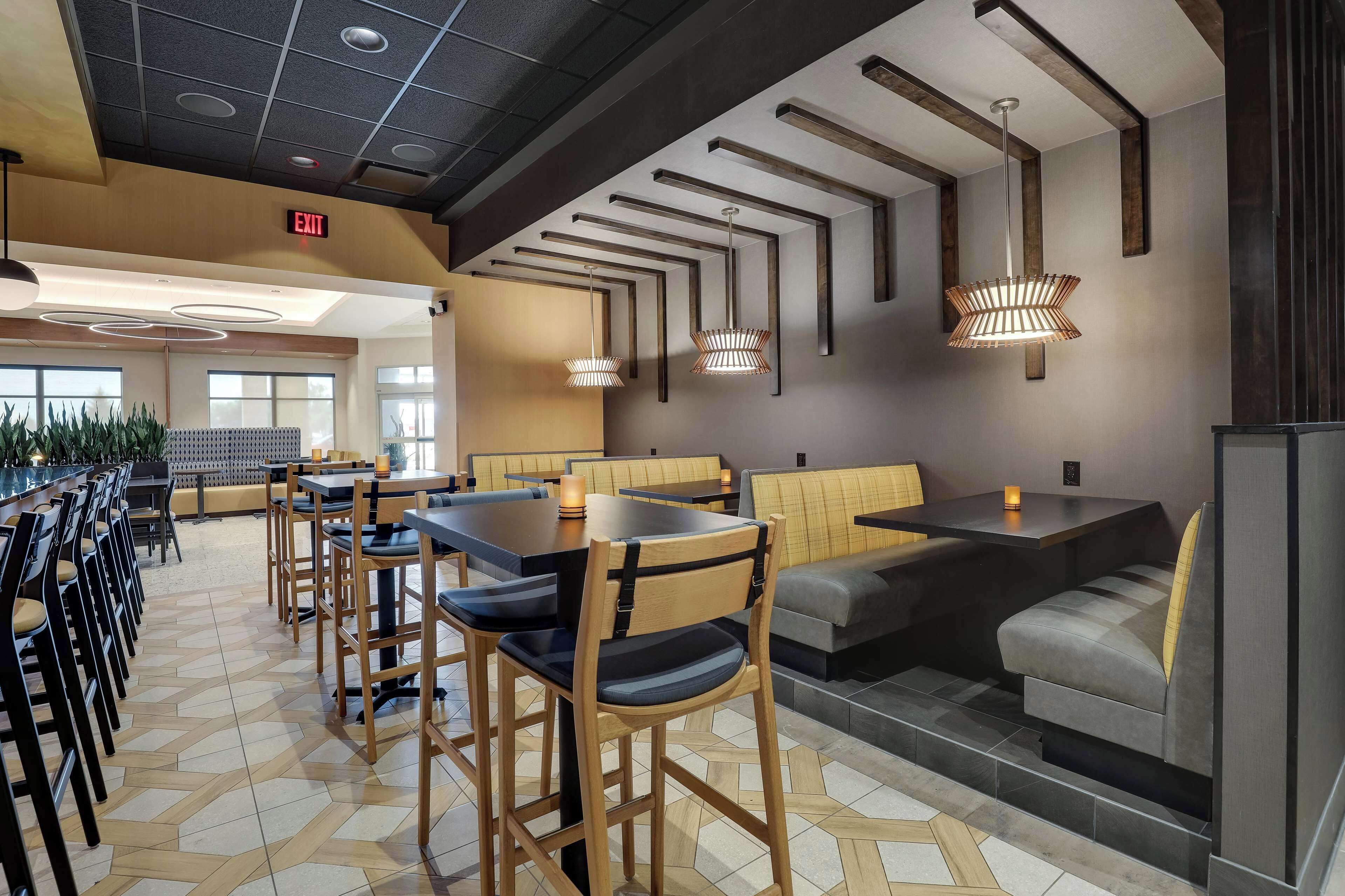 Un restaurante moderno con sillas y mesas de madera, suelo estampado e iluminación colgante.