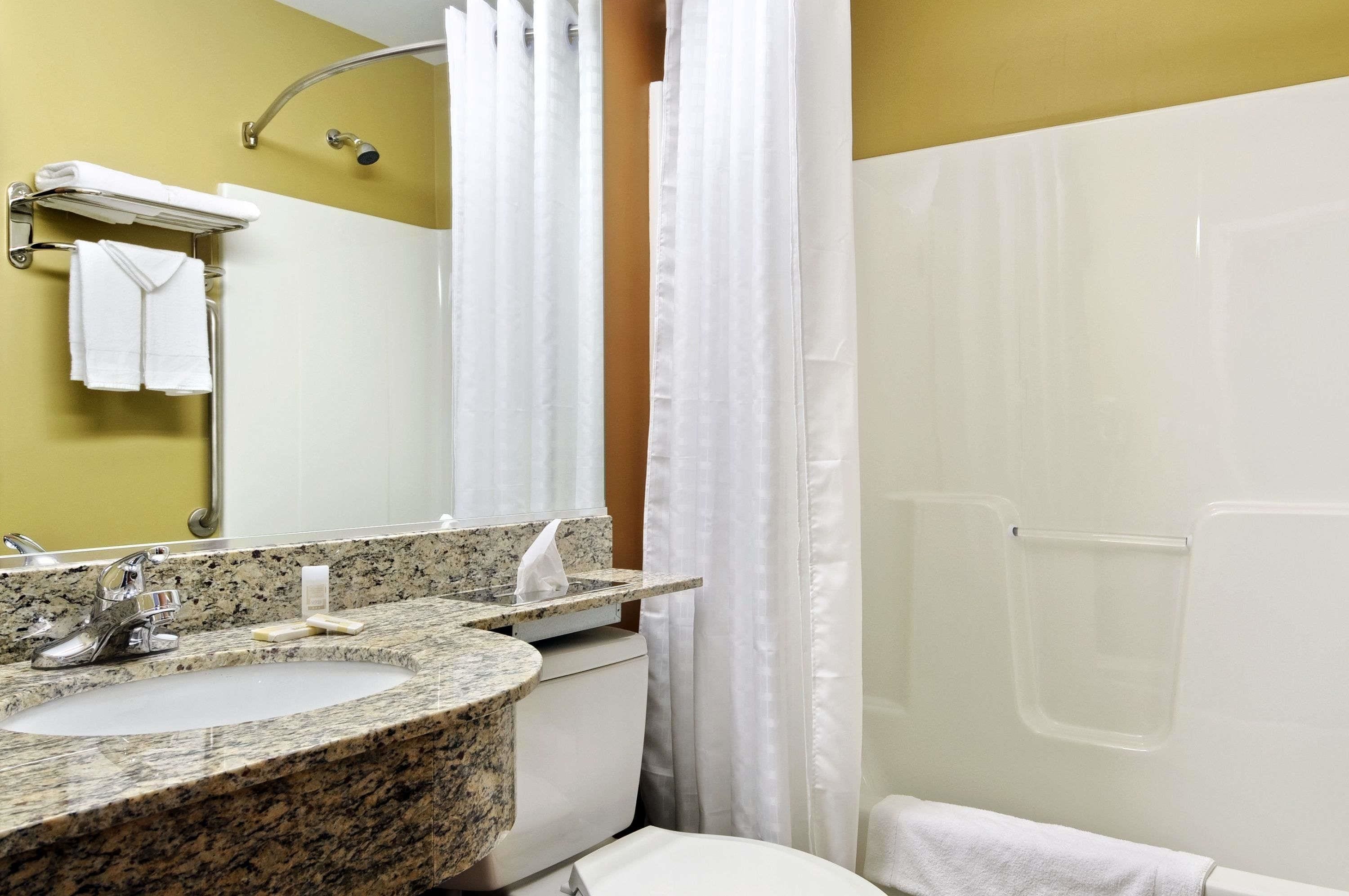A bathroom with a granite sink, a mirror, a towel rack, and a shower curtain.