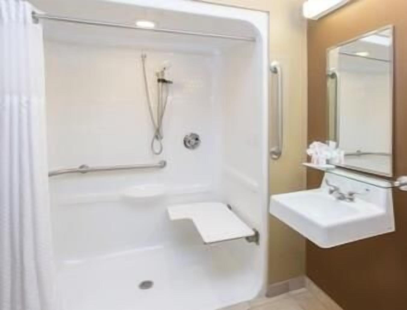 A bathroom with a walk-in shower, grab bars, a sink, and a mirror.