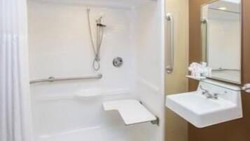 Ein Badezimmer mit begehbarer Dusche, Haltegriffen, einem Waschbecken und einem Spiegel.