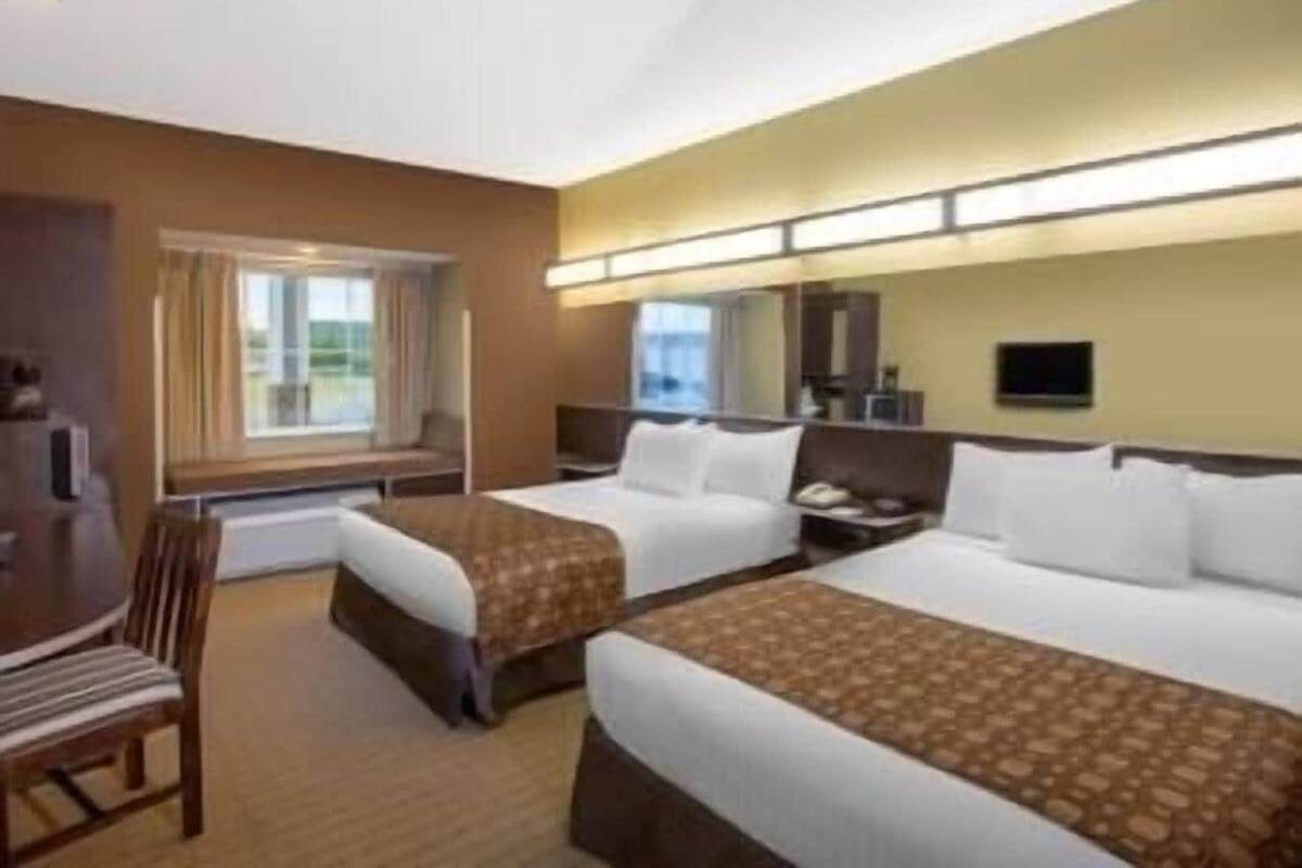 Une chambre d’hôtel avec deux lits, un bureau, une chaise, une télévision et une fenêtre avec des rideaux.
