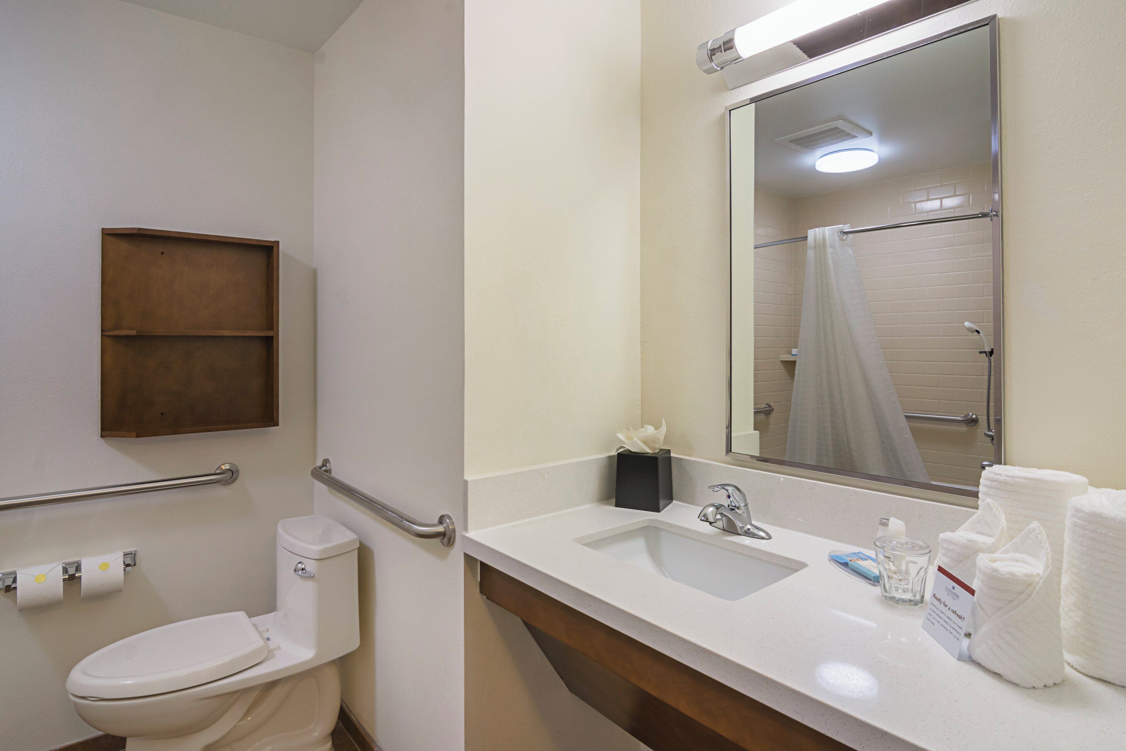 A bathroom with a toilet, a sink, a mirror, a towel dispenser, and a shower curtain.