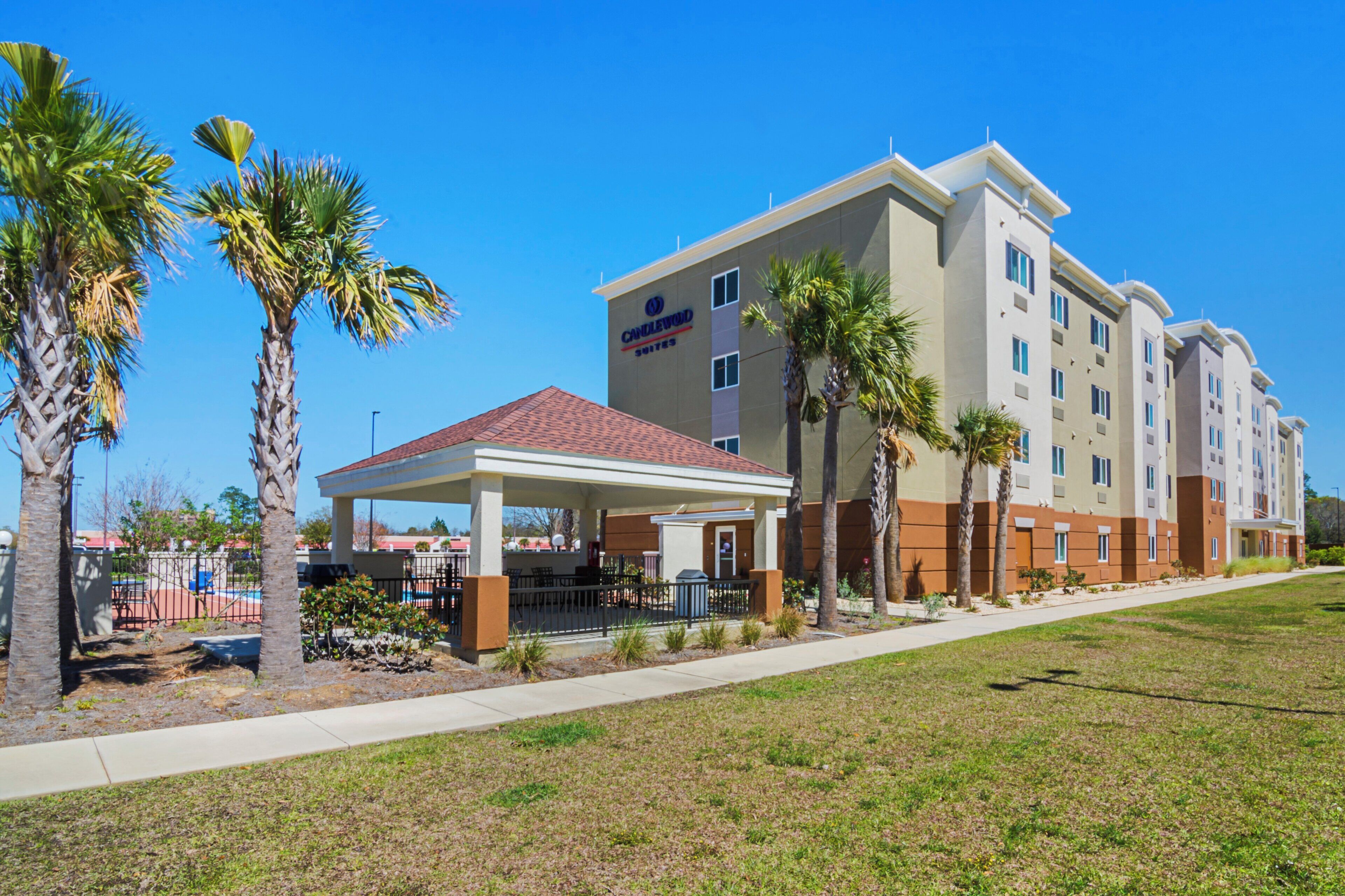 A hotel with a covered outdoor area, palm trees, and a clear blue sky.