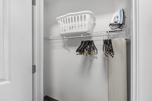 Un armario con una percha, una cesta blanca para ropa y un planchador en un estante.