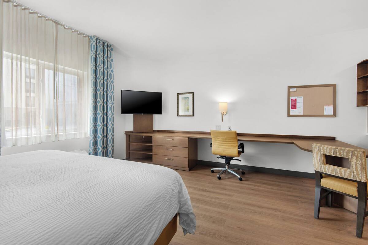 Ein Hotelzimmer mit einem Bett, einem Schreibtisch, einem Sessel, einem Fernseher und einem Korkbrett.