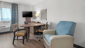 A hotel room with a desk, two chairs, a television, and a window with curtains. - Candlewood Suites Pensacola - University Area by IHG (Pensacola)