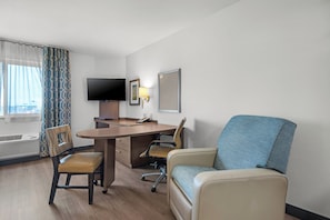 Une chambre d’hôtel équipée d’un bureau, de deux chaises, d’une télévision et d’une fenêtre avec des rideaux.