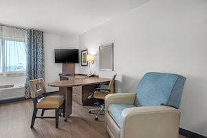 Habitación de hotel con escritorio, dos sillas, televisor y ventana con cortinas.
