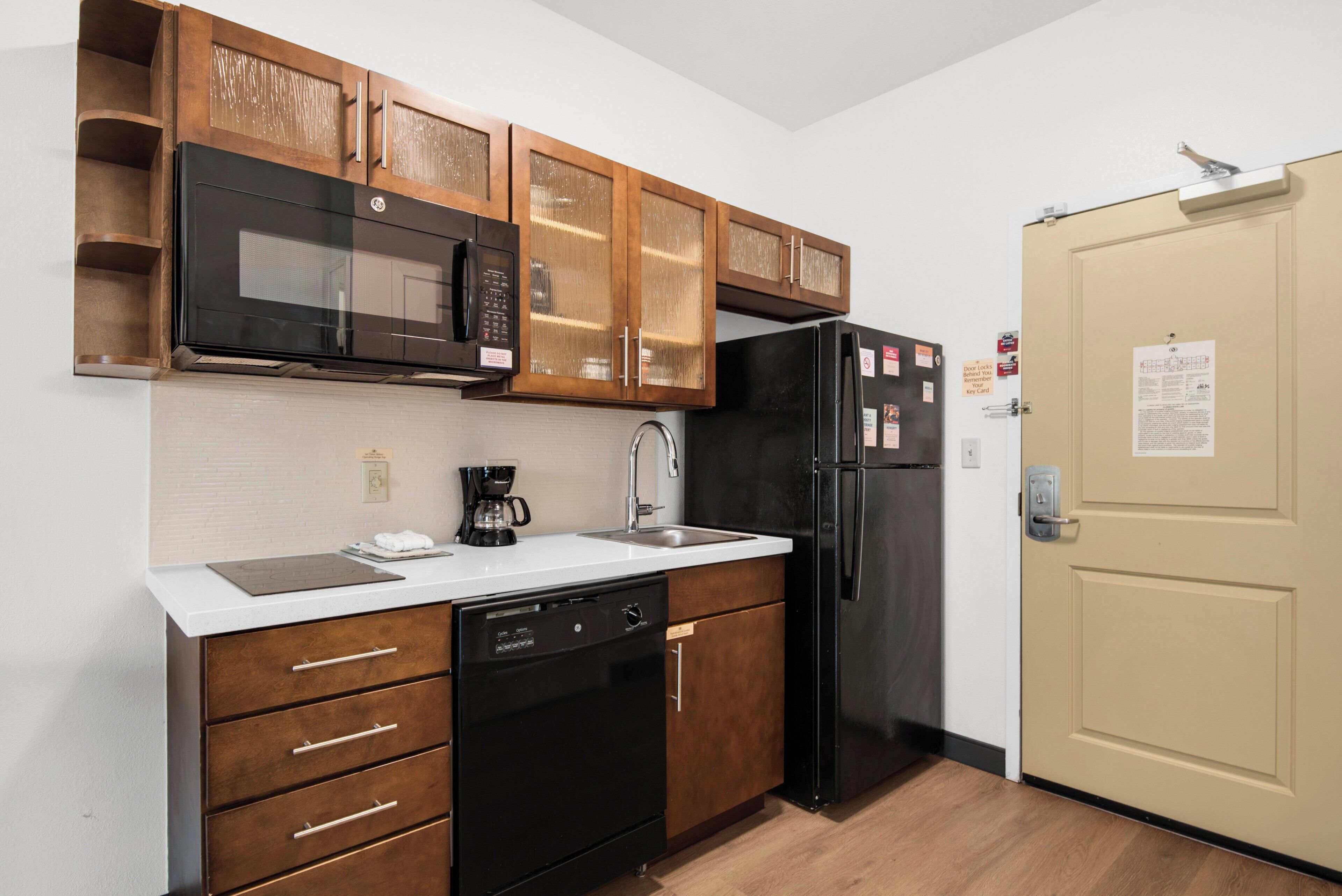 A compact kitchen with wooden cabinets, a black microwave, a coffee maker, and a refrigerator.
