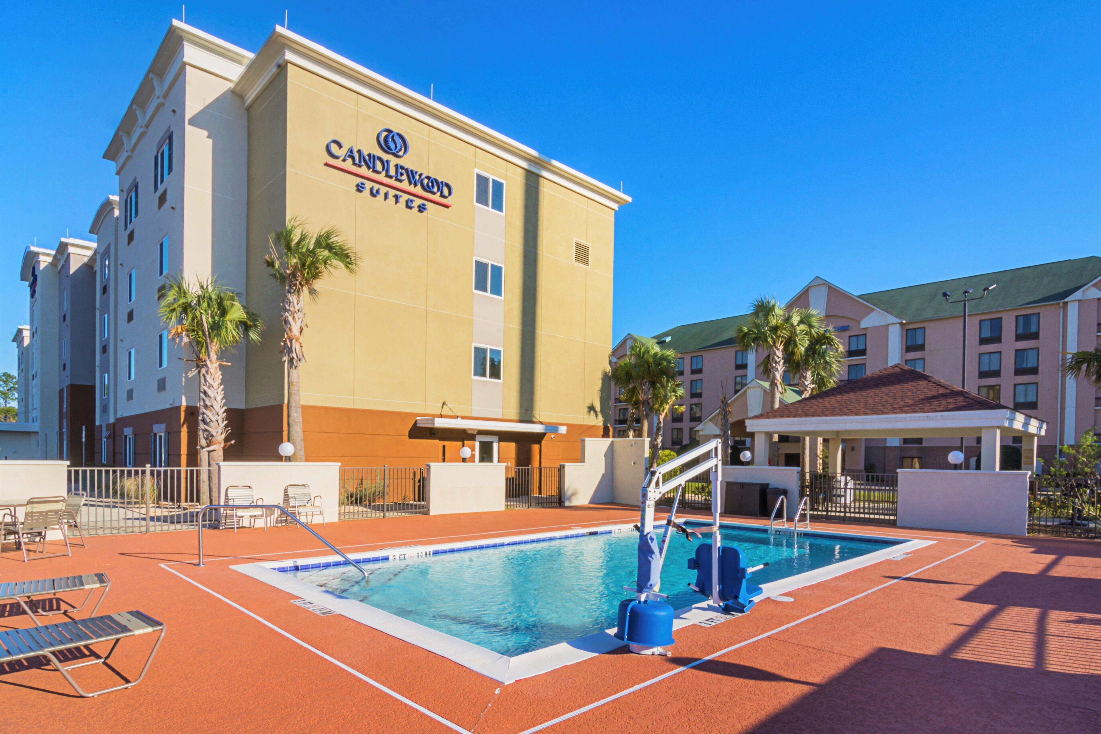 A hotel with a swimming pool, lounge chairs, and palm trees.