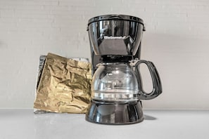 Une machine à café dotée d’une verseuse en verre transparent et d’une anse, posée sur un plan de travail.