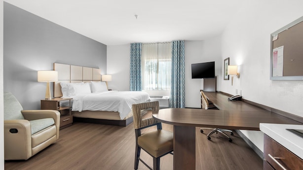 A hotel room with a bed, a desk, a chair, a TV, and a window with curtains. - Candlewood Suites Pensacola - University Area by IHG (Pensacola)