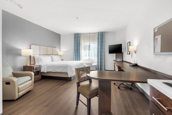 Une chambre d’hôtel avec un lit, un bureau, une chaise, une télévision et une fenêtre avec des rideaux.