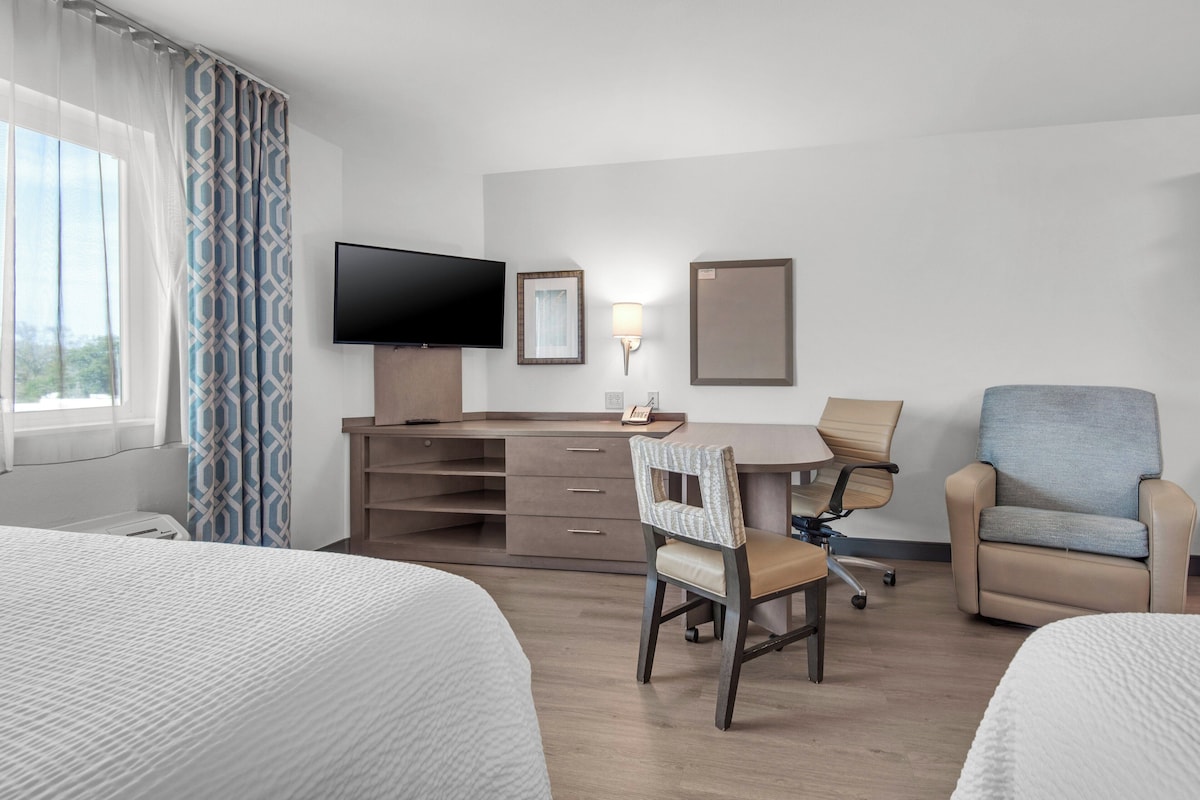 Une chambre d’hôtel avec un lit, un bureau, une chaise, une télévision et une fenêtre avec des rideaux.