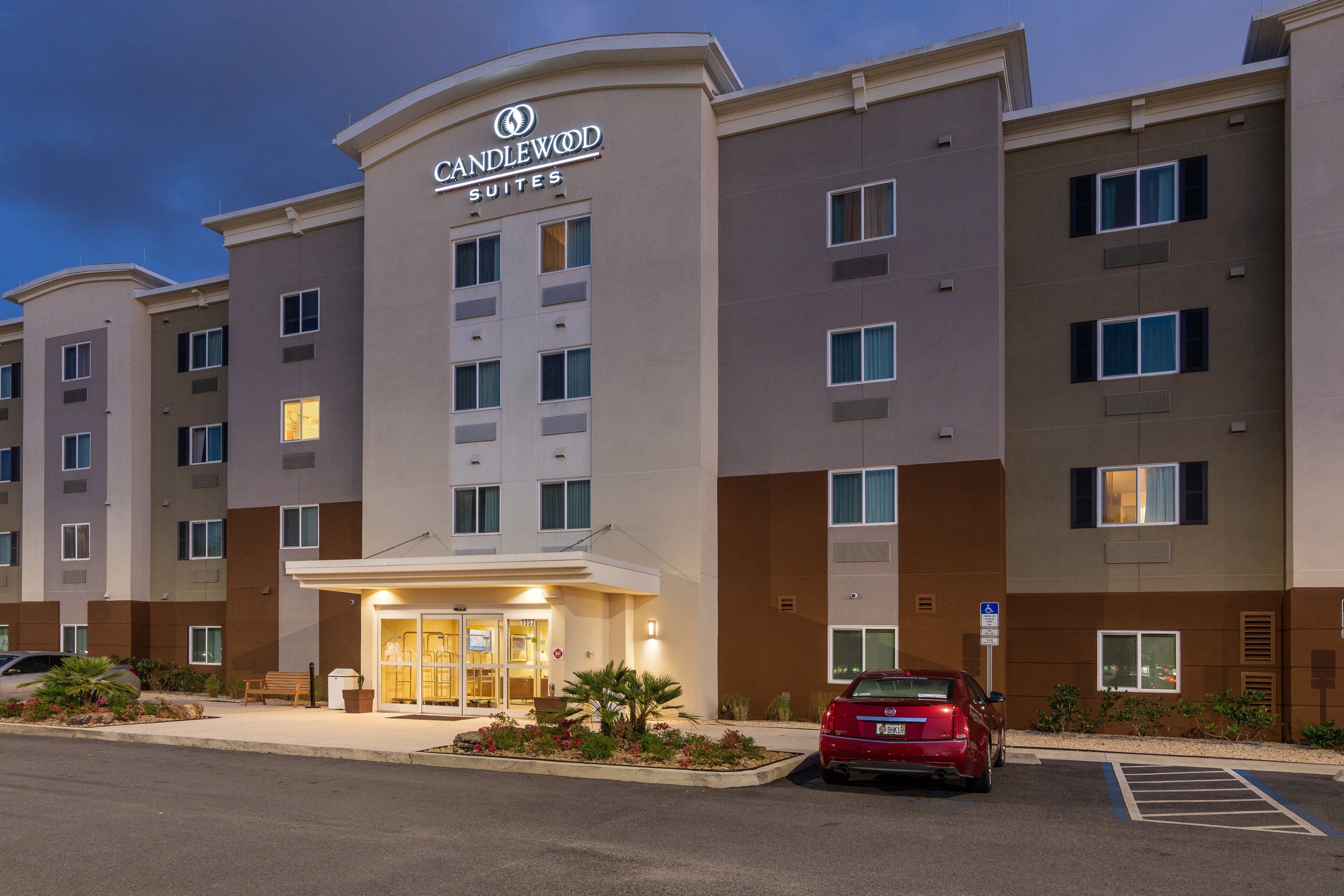 A hotel with a modern facade, multiple floors, and a parking area with a red car.