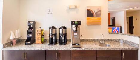 Una cocina de hotel con estación de café que incluye varias cafeteras y un dispensador de agua.