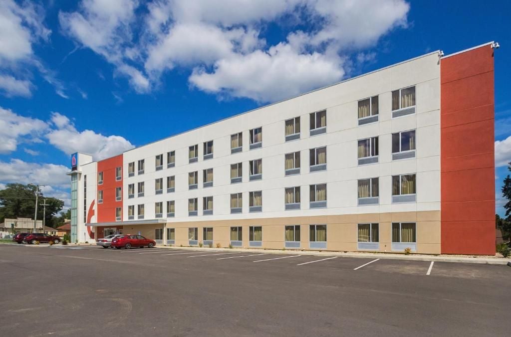 Un hôtel à plusieurs étages, doté d’une façade sobre, d’un parking à l’avant et surplombant un ciel d’un bleu limpide.