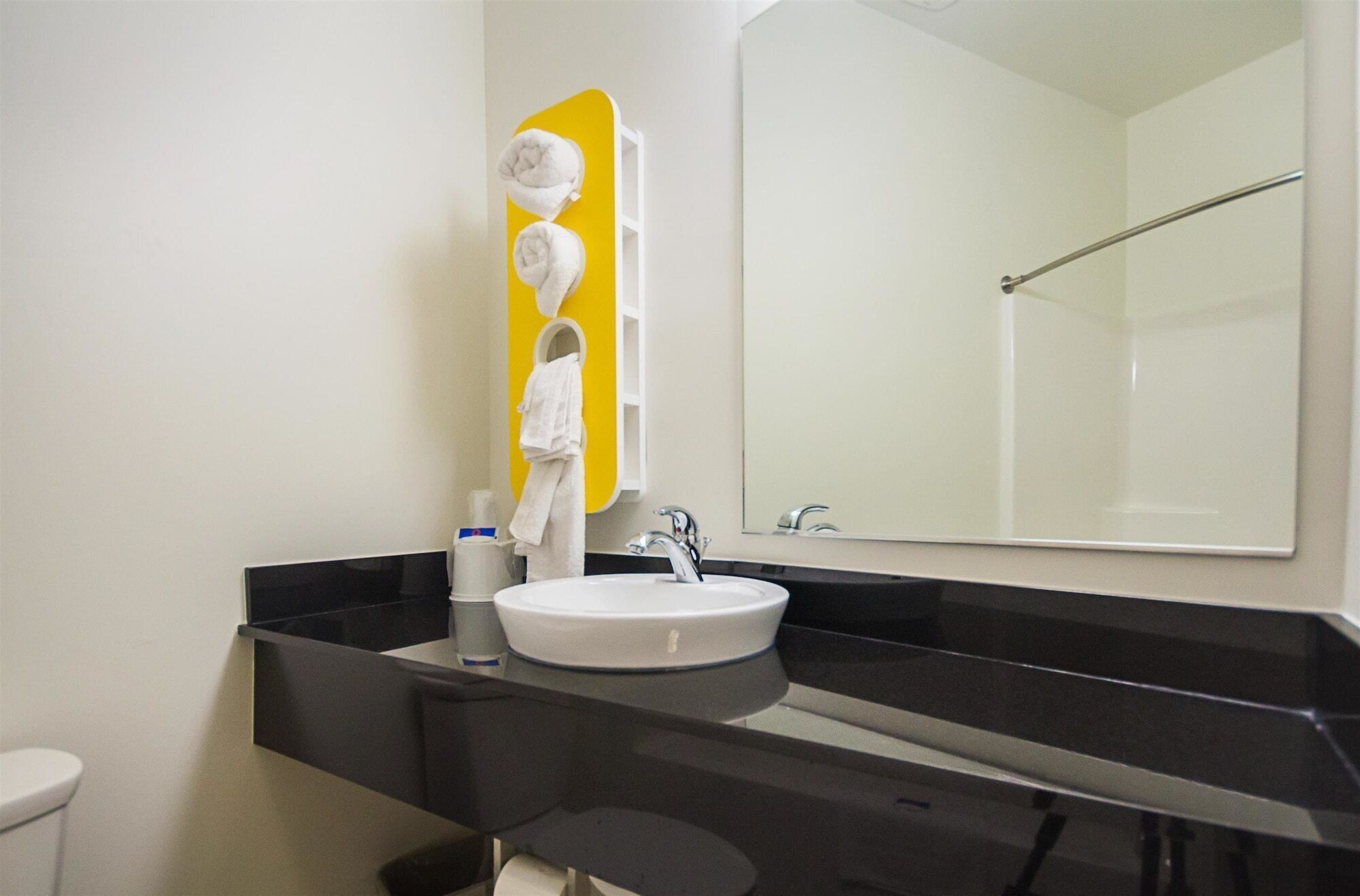 A modern bathroom with a black countertop, a white sink, and a mirror with a yellow accent.