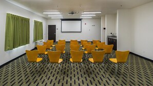A conference room with rows of yellow chairs, a projector screen, and a small kitchenette. - Days Inn by Wyndham South Bend / Notre Dame (South Bend)