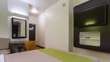 A hotel room with a bed, a desk, a chair, a mirror, a television, and a small shelf.