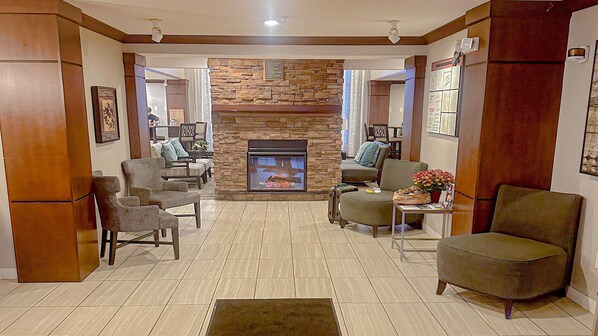 A living room with a stone fireplace, seating, and a small table with flowers. - Staybridge Suites Elkhart North by IHG (Elkhart)