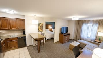 A compact hotel room with a kitchenette, a bed, a TV, a sofa, and a small dining area.