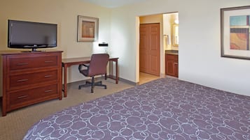 Habitación de hotel con cama, escritorio, silla, televisión, cómoda y puerta que da a un baño.