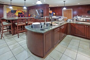 A kitchen area with a buffet setup, including a refrigerator, coffee station, and various food items. - Staybridge Suites Elkhart North by IHG (Elkhart)