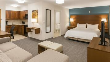 A hotel room with a bed, a desk, a chair, a sofa, a small table, a TV, and a bathroom visible through an open door.