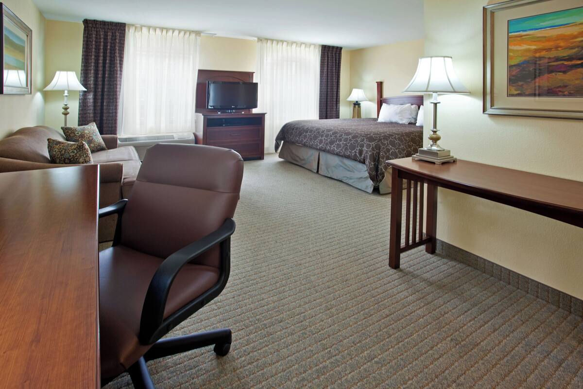 A hotel room with a bed, a desk, a chair, a television, and two lamps.