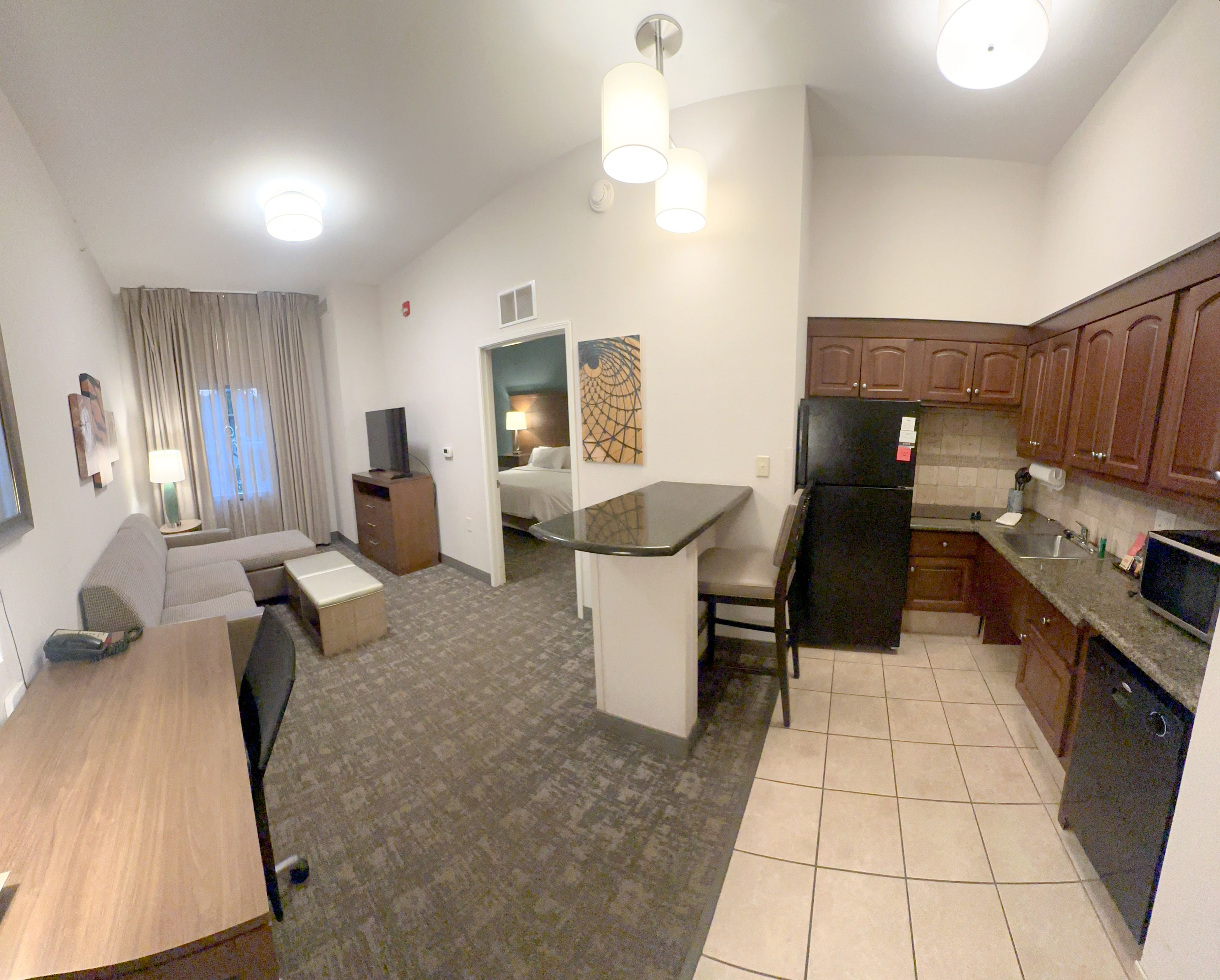 A compact hotel room with a kitchenette, a dining area, and a living space.