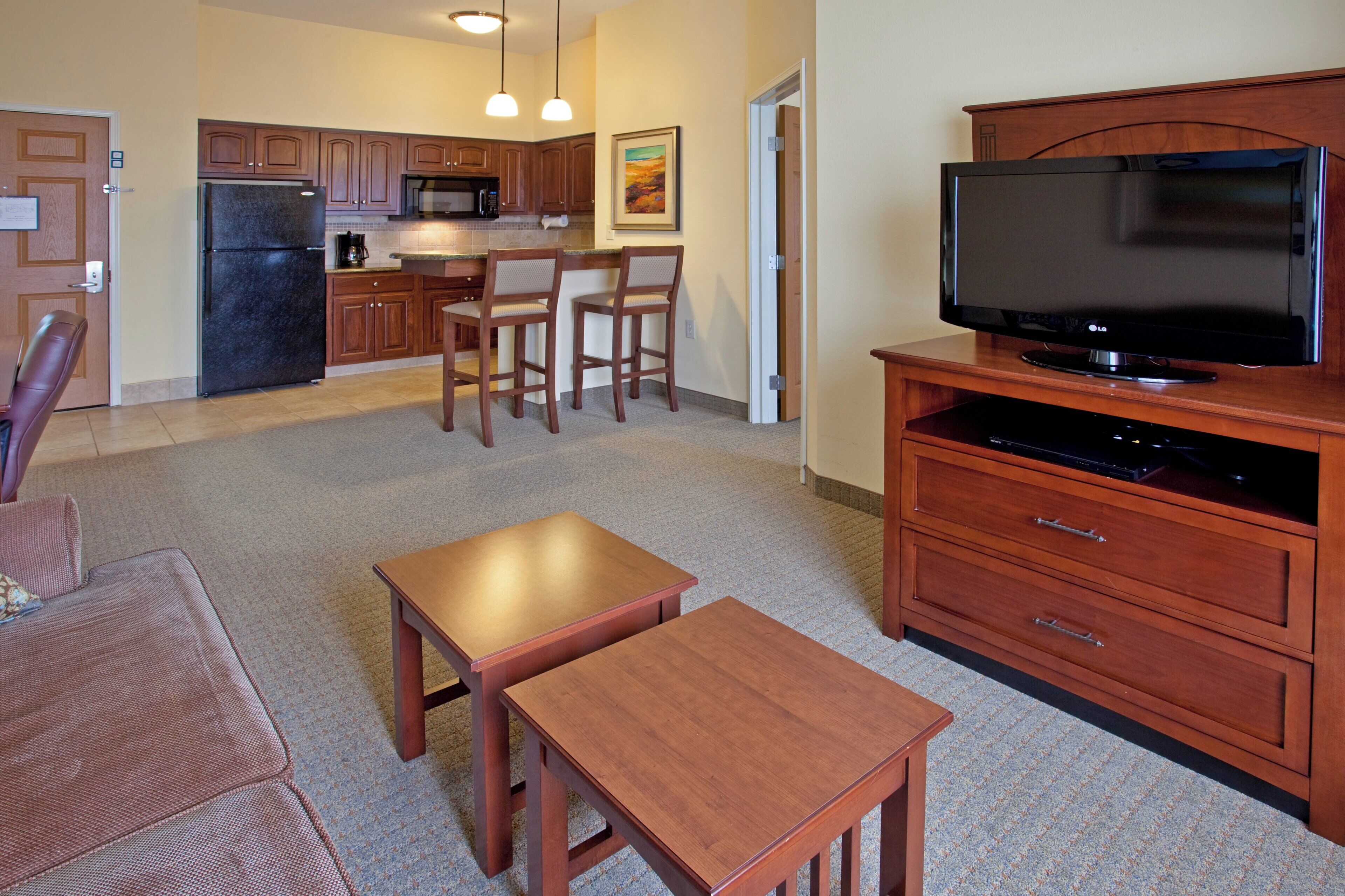 A compact living space with a kitchenette, a flat-screen TV, a dining area with two chairs, and a small wooden table.