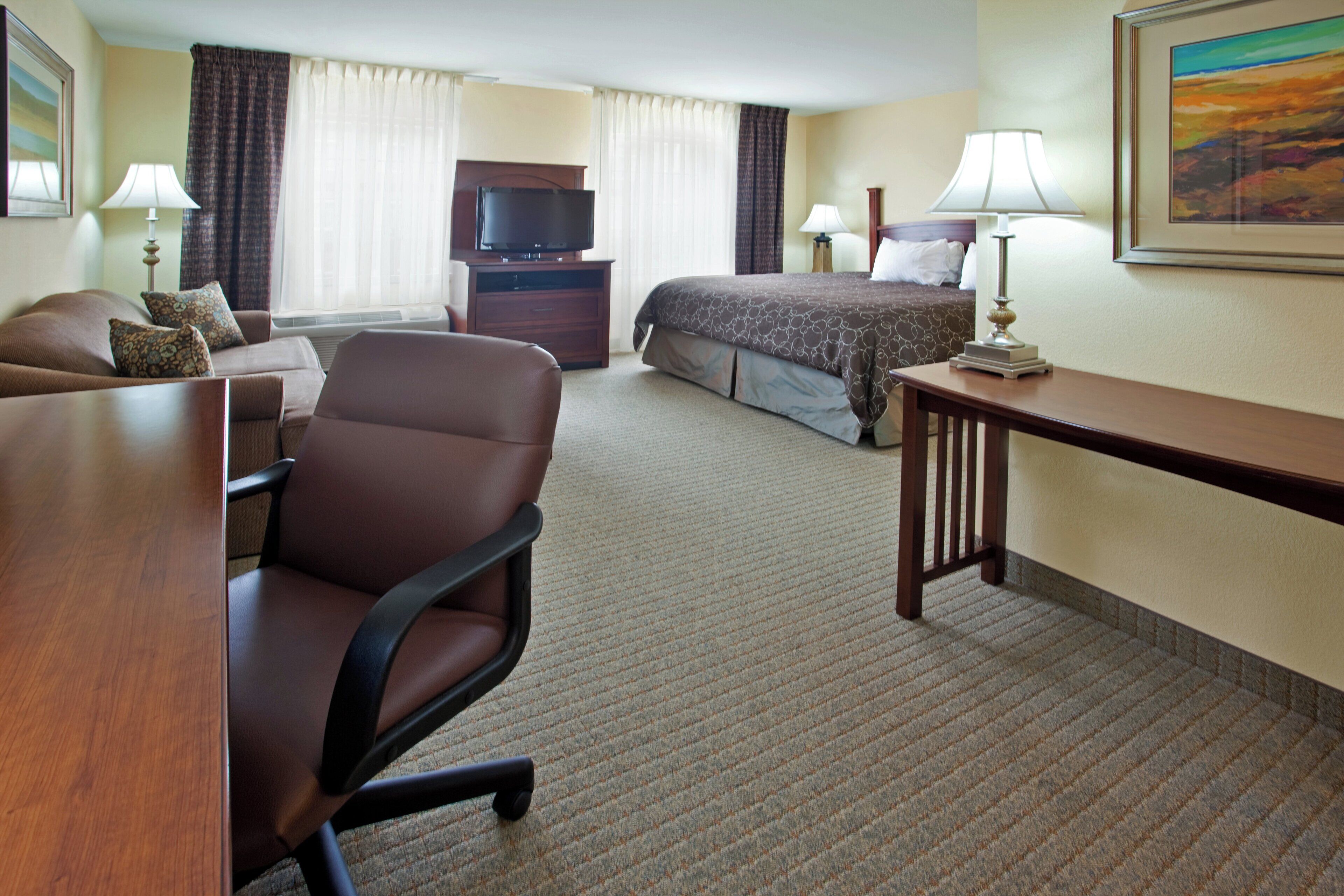 A hotel room with a bed, a desk, a chair, a television, and two lamps.