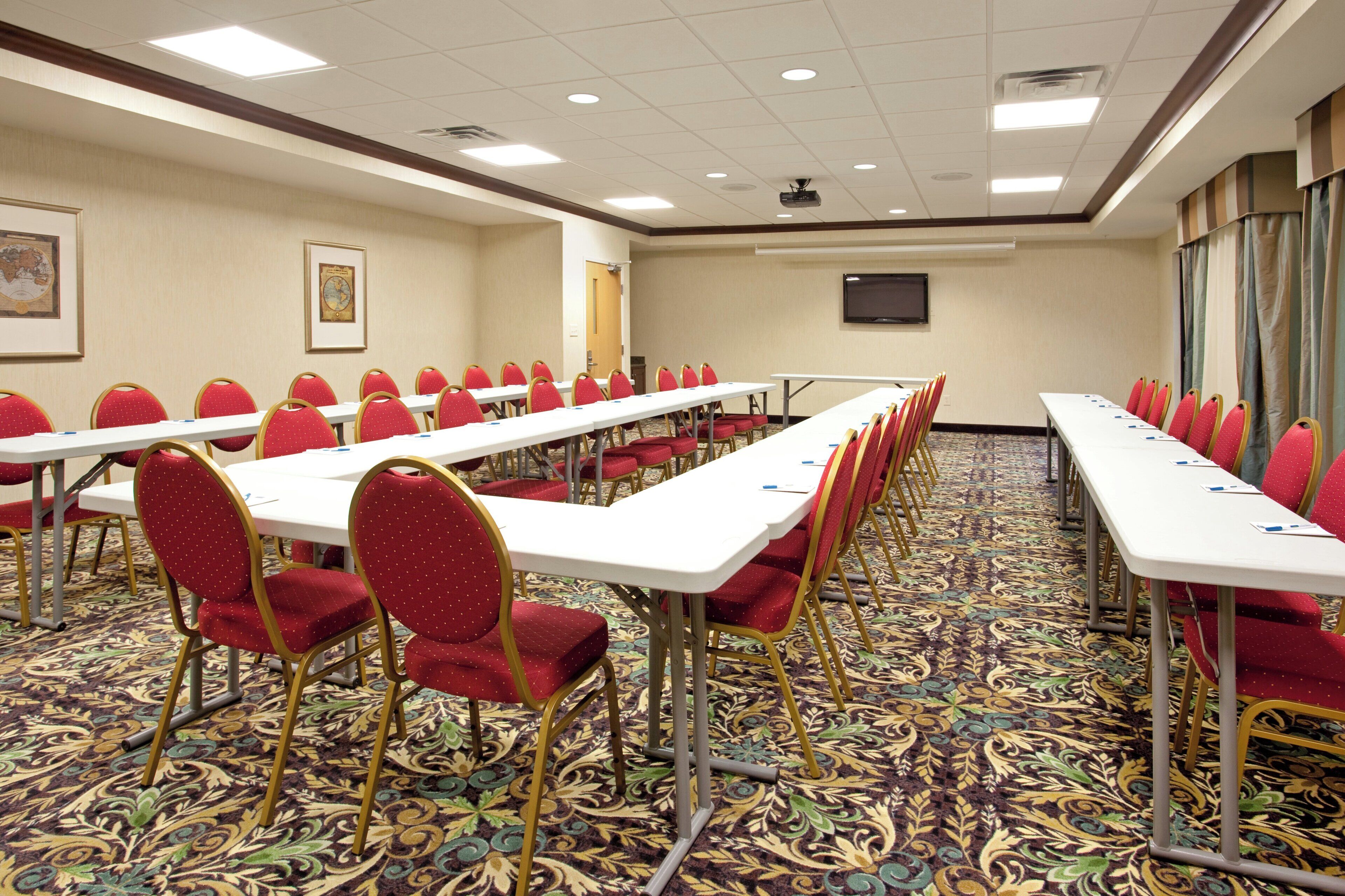 A conference room with rows of tables and chairs, a projector screen, and a carpeted floor.