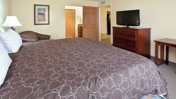 A hotel room with a large bed, a television, a dresser, and a door leading to a hallway.