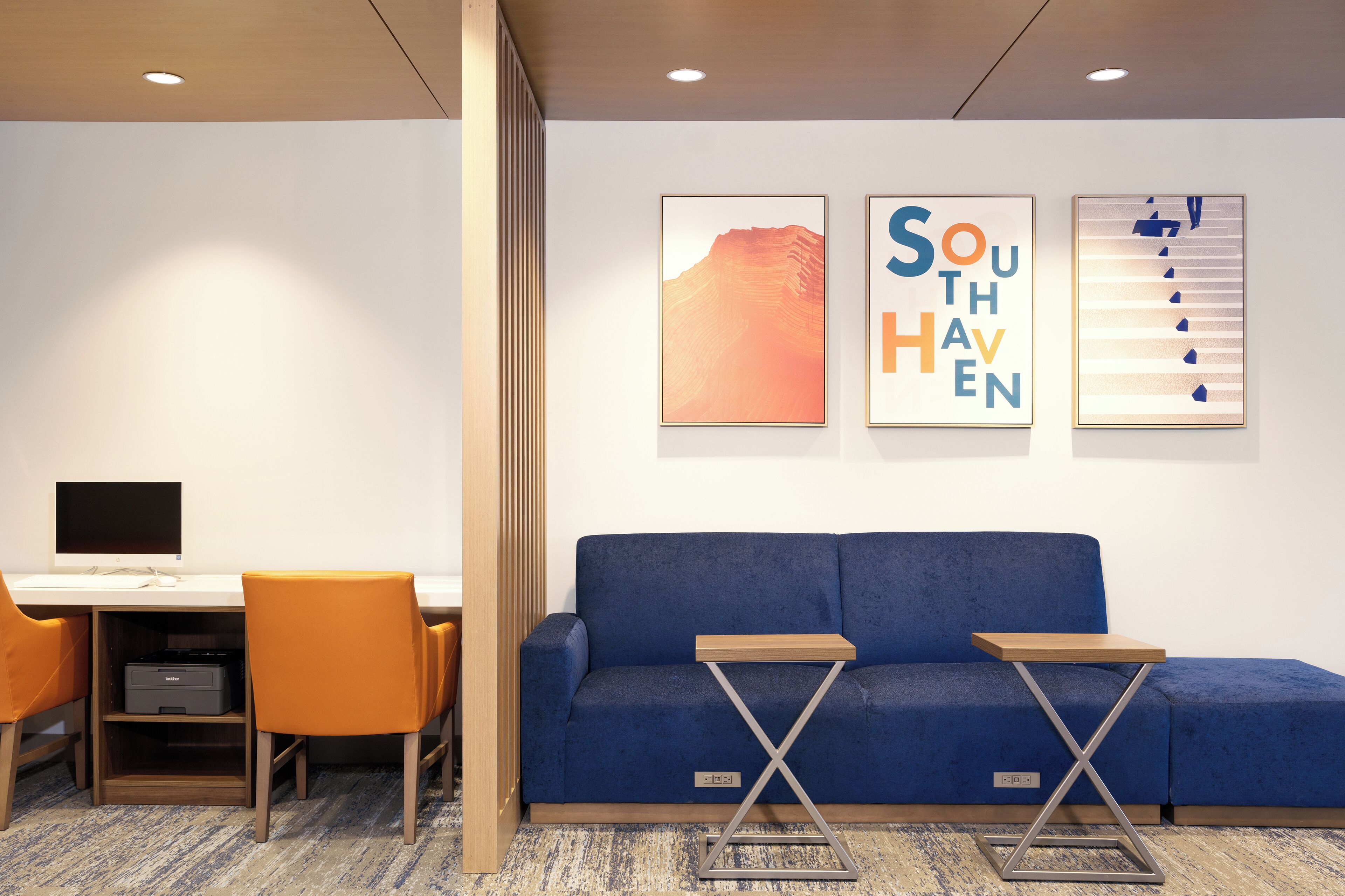 A modern hotel room with a blue sofa, a desk with a computer, and two small tables.