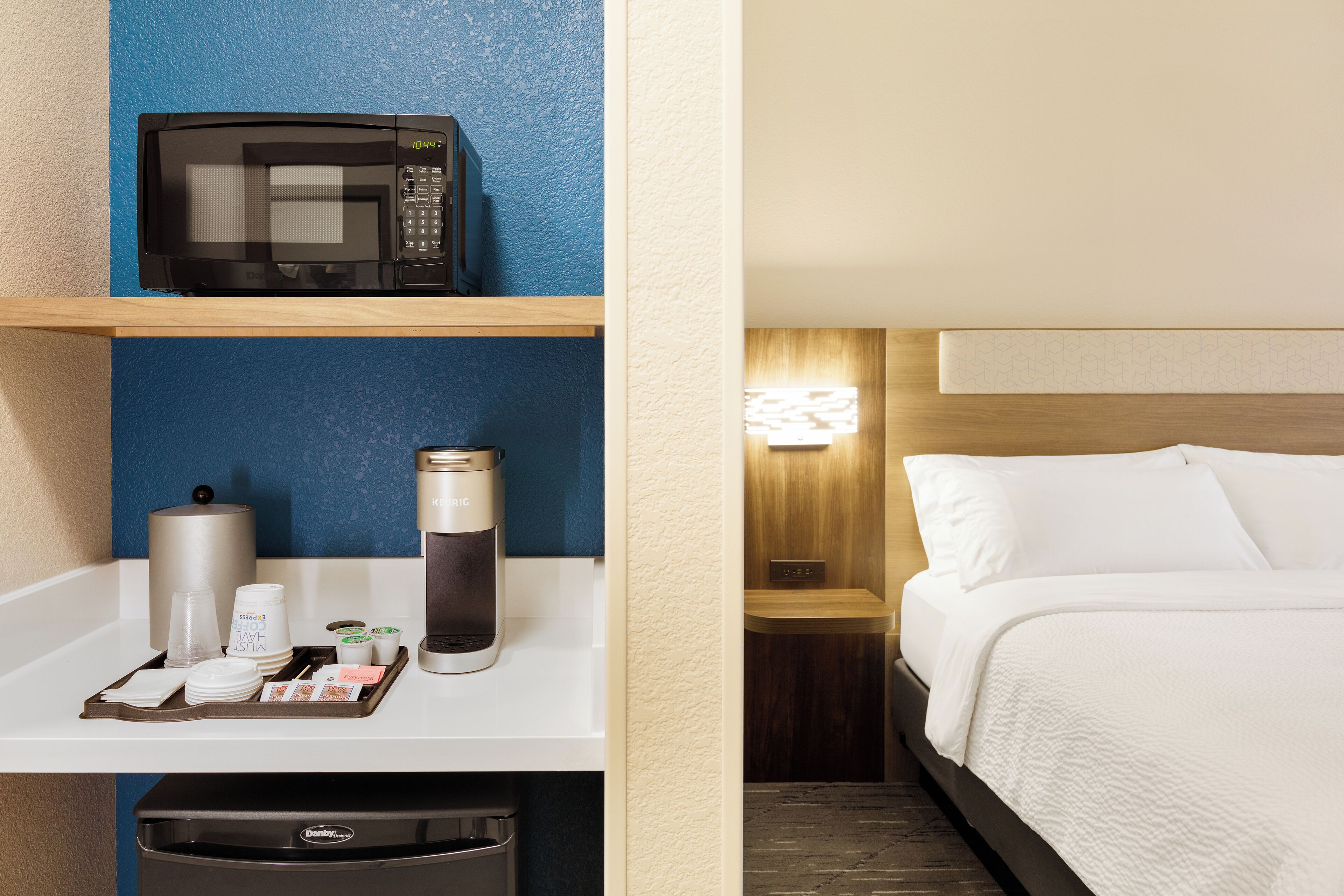 Quarto de hotel com micro-ondas numa prateleira, cafeteira e lixeira.